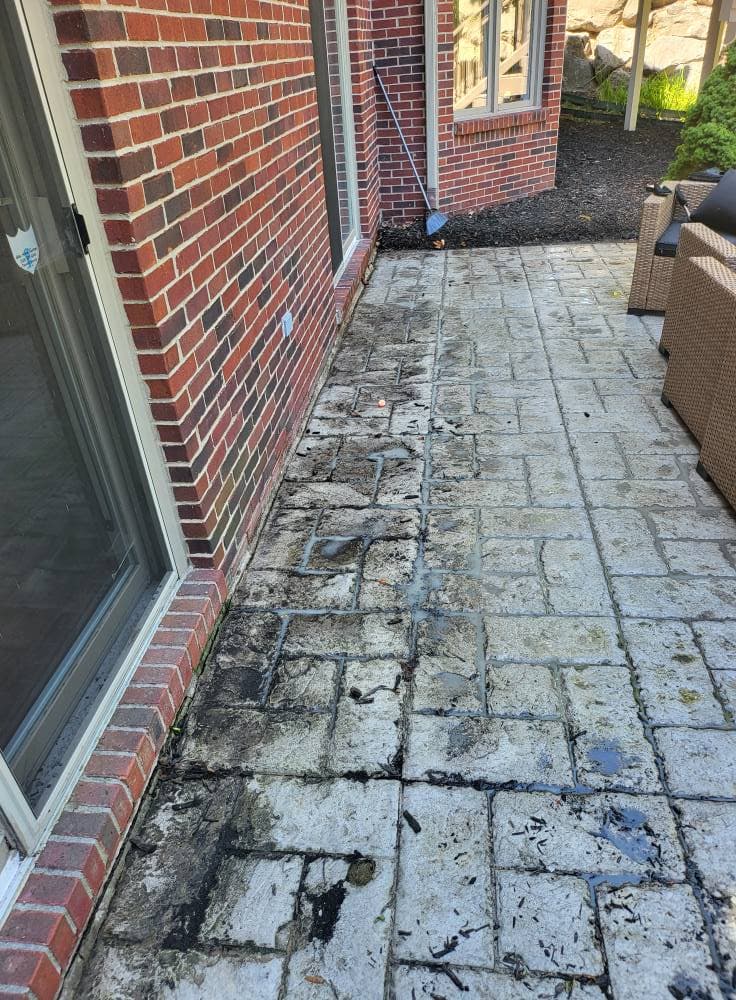 Paver patio surface with dark staining and weathering before cleaning