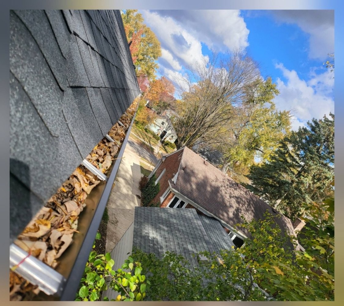 Gutters full of fall leaves before cleaning with dull sky